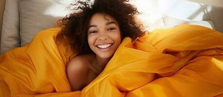 Happy African girl on a bed with copy space laughing and playing with a blanket while looking at the camera photo