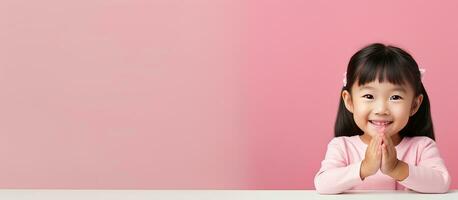 Little Asian girl sitting and presenting open hand palm with copy space on pink background photo