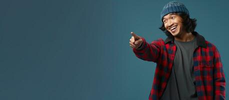 Asian man in beanie hat and flannel shirt energetically pointing down on blue background photo