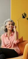 Happy middle aged lady chatting on the phone with a joyful expression seated on a couch at home and empty space available for writing photo