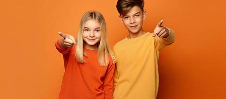 White teenage girl with boy student pointing at empty space separated by orange backdrop Positive update discounted suggestion collaborate academically ed photo