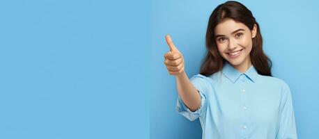 Vertical portrait of a young woman on a blue background gesturing approval and pointing to an empty space overhead for commercial promotion photo