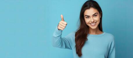 Vertical portrait of a young woman on a blue background gesturing approval and pointing to an empty space overhead for commercial promotion photo