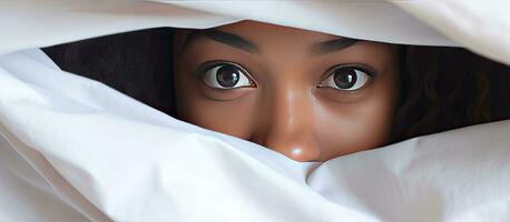 African girl hiding face under blanket while lying in bed photo