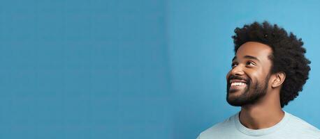 Side view of young African American man smiling and looking aside isolated on blue background with copy space photo