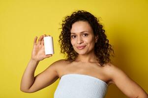 hermosa sonriente medio Envejecido mujer participación cosmético producto botella aislado en amarillo antecedentes con Copiar espacio foto