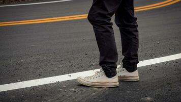 hombres vistió zapatillas en pie en pavimentado carreteras con amarillo y blanco tráfico líneas cruce el montañas. foto