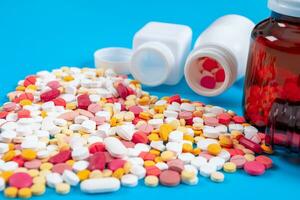 Medical pills and tablets spilling out of a drug bottle on blue background photo