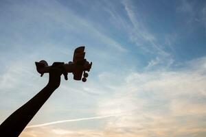 Silhouette of happy children playing a wooden toy plane on the sunset sky background. photo