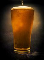 verter cerveza dentro un vaso en oscuro fondo.luz cerveza en un vaso,borrador.fresco ligero cerveza.de cerca. foto