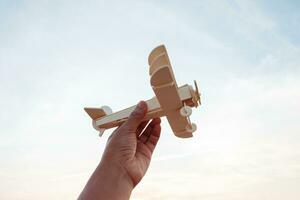 Freedom concept, human hand holding wooden plane on the sunset sky background photo