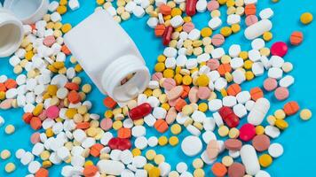 Medical pills and tablets spilling out of a drug bottle on blue background photo