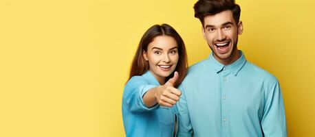 Two enthusiastic friends in casual attire isolated in front of a yellow backdrop display approval by pointing and showing thumbs up photo