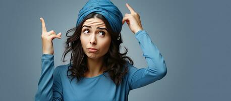 Puzzled Arab woman in blue pajama with open palm and pointing finger to forehead photo