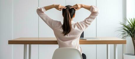 A female caucasian entrepreneur or secretary in an office tries to relax her shoulders and back by stretching her hands while wearing a white shirt photo