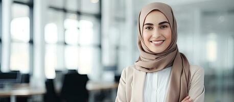 Confident young Muslim woman in modern office wearing a headscarf smiling at the camera waist up photo