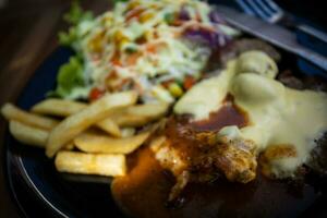 Cheese Pork Steak on a Black Plate with Vegetable Salad photo