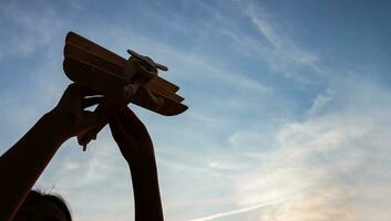 Silhouette of happy children playing a wooden toy plane on the sunset sky background. photo