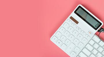 Top view female workplace, Computer keyboard, white calculator and glasses on a bright pink background. photo