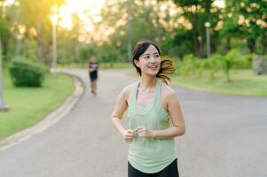 Fit Asian young woman jogging in park smiling happy running and enjoying a healthy outdoor lifestyle. Female jogger. Fitness runner girl in public park. healthy lifestyle and wellness being concept photo