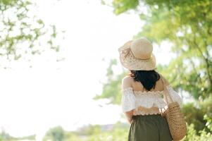 Portrait of asian young woman traveler with weaving hat and basket and a camera on green public park nature background. Journey trip lifestyle, world travel explorer or Asia summer tourism concept. photo