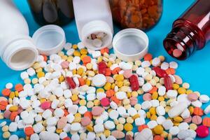 Medical pills and tablets spilling out of a drug bottle on blue background photo