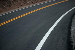 The asphalt road has yellow and white traffic lines crossing the mountains. photo