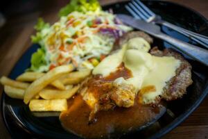 queso Cerdo filete en un negro plato con vegetal ensalada foto