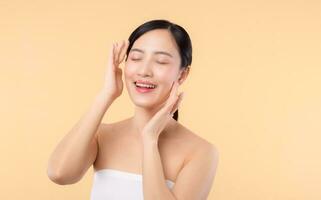 Beautiful girl asian model touching fresh glowing hydrated facial skin on beige background closeup. Beauty face young woman with natural makeup and healthy skin portrait. Skin care concept photo