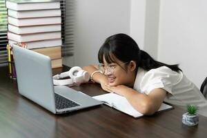 estudiante niña contento estudiando en línea, espalda a colegio concepto. joven mujer estudiante ocupado estudiar hacer notas en cuaderno y utilizando ordenador portátil concentrado en línea formación curso tecnología educación. foto