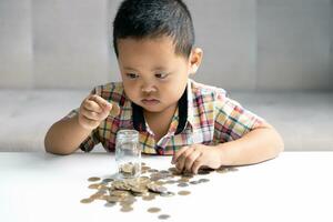 preescolar niño aprendizaje a calcular personal presupuesto, gestionar finanzas, jugando inversión, contabilidad. enfocado colegio niño ahorro dinero para compra, poniendo efectivo en rosado cerdito banco a hogar. foto