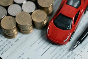 Miniature car model and Financial statement with coins. Finance and car loan, saving money for a car concepts. Car loan, money, banknote on agreement document or car insurance application form. photo