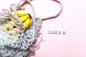Vegan inscription from wooden letters. Flat lay zero waste shopping bag with fruits on pink background photo