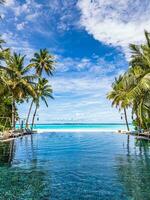 Tropical beach resort pool in a luxurious beachfront hotel resort at sunset enjoying perfect beach holiday vacation. Exotic travel destination. Tranquil idyllic nature, blue sea, green palm trees photo