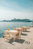 Greece, Santorini. Restaurant with tables in seafront of Aegean sea on Santorini Cyclades island with cruise ships in the background. Famous Europe travel tourism destination for summer vacation photo