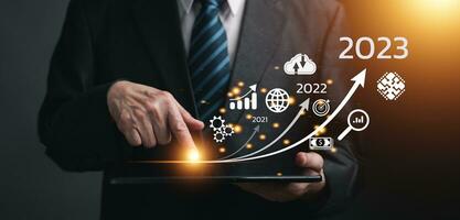 Businessman touching on tablet, line for increasing arrow from 2022 to 2023 for new business, Startup concept with icon business and network connection on modern virtual interface from digital tablet. photo
