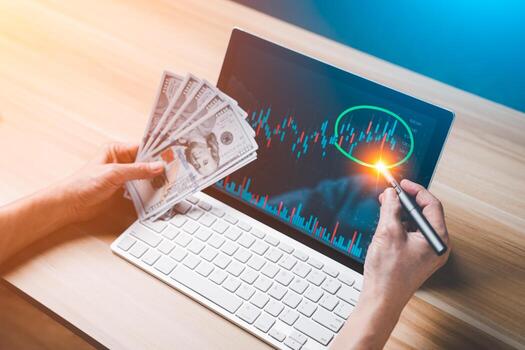 Trader investor using pen circle on the Laptop computer or tablet screen show financial chart and hold banknote. Stock market, cryptocurrency, Bitcoin graphs. Technology investing for money concepts. photo