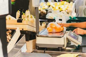 Grocery Store staff weighing oranges in plastic bag on digital scales. photo