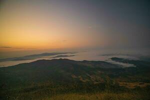 The stunning view from a tourist's standpoint as they go down a hill on a foggy trail with a hill and a background of a golden sky in Phu Langka Forest Park in Phayao, Thailand. photo