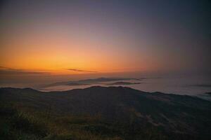 The stunning view from a tourist's standpoint as they go down a hill on a foggy trail with a hill and a background of a golden sky in Phu Langka Forest Park in Phayao, Thailand. photo
