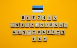 August 20, Estonia Independence Restoration Day, flag of Estonia, minimalistic banner with the inscription in wooden letters on an orange background photo