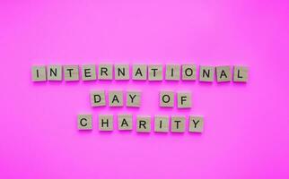 September 5, International Day of Charity, minimalistic banner with the inscription in wooden letters on a pink background photo