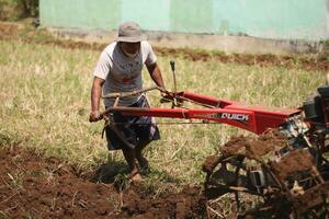 Magelang Indonesia.07302023-a farmer is plowing a field with a modern tool in the form of a tractor. photo