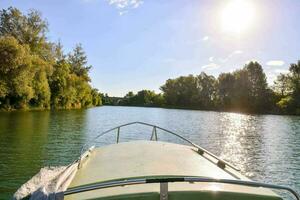 a boat on a river with trees and sun shining photo