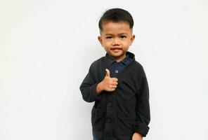 A smiling toddler boy looks at the camera raising his hands to show thumbs up, isolated on white background photo