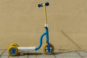 a small blue and yellow scooter sitting against a wall photo