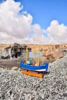 a toy boat on the rocks in front of a mountain photo