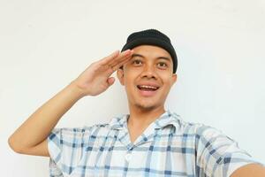 Happy adult man wearing pajamas and beanie cap smiling while saluting looking at camera. Isolated on white background photo