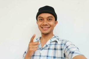 Smiling adult man wearing pajamas and beanie cap pointing with his finger while looking at camera. Isolated on a white background photo