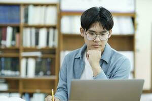 joven Universidad estudiante utilizando ordenador portátil para en línea aprendiendo, buscando y aprendizaje a biblioteca. foto